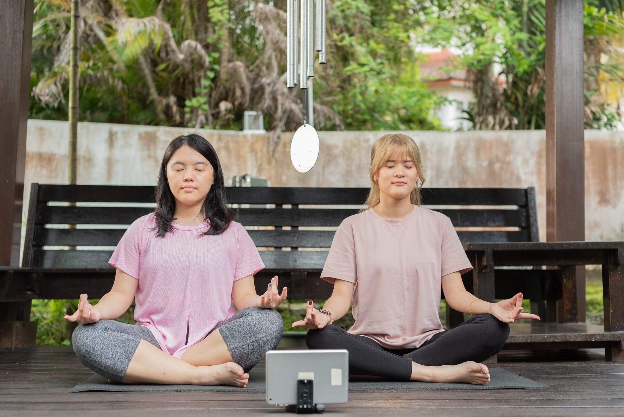 Two women meditating together in a peaceful outdoor setting.
